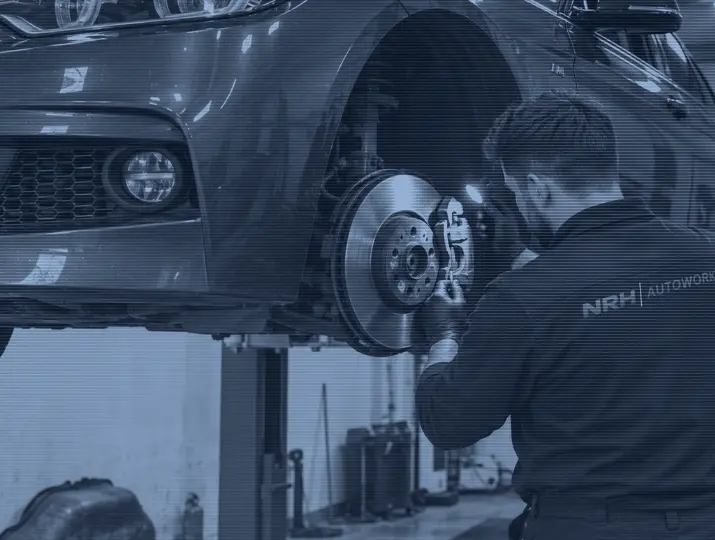A mechanic inspecting a front brake disc and caliper with the wheel removed