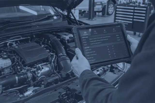 A diagnostic tablet showing fault codes and live data, held over an engine bay in our workshop