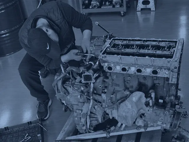 A mechanic working on an engine that has been taken out of the vehicle and part stripped, on the workshop floor