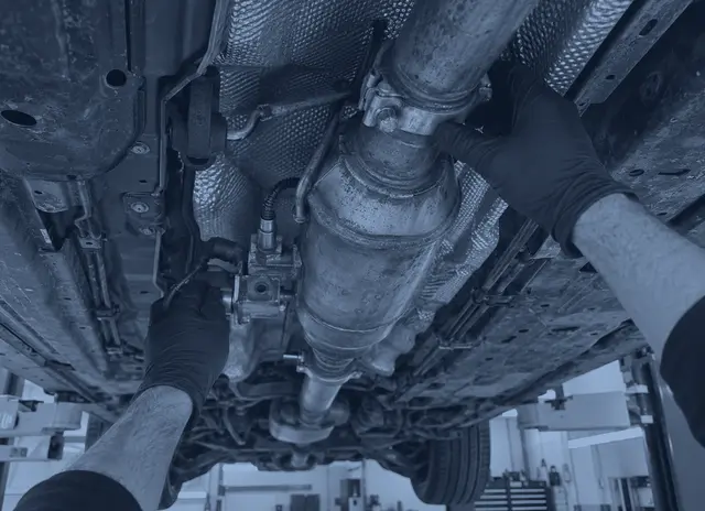 A mechanic checking an exhaust joint and sensor underneath a car on the lift