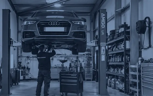 A car raised on a two post lift while a mechanic works underneath it in our workshop